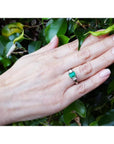 18k white gold three stone ring with a 1.38 ct emerald and two princess cut diamonds on a hand.