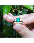 18k white gold three-stone ring with a vibrant emerald and two princess-cut side diamonds.