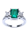 A white gold ring with emerald and side diamonds on a white background
