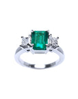 18k white gold three-stone ring with a rectangular emerald and two princess-cut side diamonds.