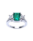 18k white gold three-stone ring with a rectangular emerald and two princess-cut side diamonds.
