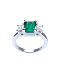 18k white gold three stone ring with a vibrant emerald and two princess cut diamonds.