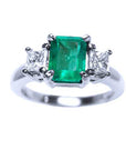 A top view of a three stone natural emerald ring with princess cut side diamonds in white gold.