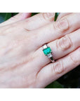 18k white gold three-stone emerald ring with princess cut side diamonds on a hand.