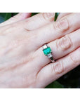 18k white gold three-stone emerald ring with princess cut side diamonds on a hand.
