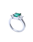 18k white gold three-stone ring with a rectangular emerald and two princess-cut side diamonds.