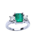 18k white gold three-stone ring with a rectangular emerald and two princess-cut side diamonds.