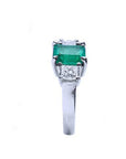 White gold ring with an emerald and a side diamond on a white background.