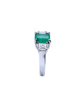 18k white gold three-stone ring with a rectangular emerald and two princess-cut side diamonds.