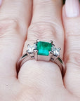 A 18k white gold three stone emerald ring on a hand.