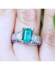 A women's Colombian emerald ring in 18k white gold and accent diamonds on a finger.