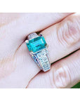 Emerald-cut 2.02 ct. Colombian emerald ring with diamonds in 18K white gold on a finger.