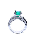 Ring with an emerald gemstone and diamond accents on a lateral position top and gallery visibles.