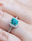 Women's cushion cut emerald ring on a hand.