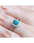 Women's 1.19 ct cushion cut emerald ring with diamond halo, set in 14K white gold on a finger.