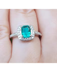 A women's emerald ring cushion cut with halo of natural diamond in white gold on a finger.