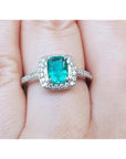 A women's emerald ring cushion cut with halo of natural diamond in white gold on a finger.