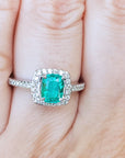Emerald ring with diamond accents on a finger.