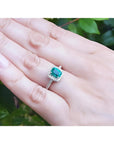 Women's 14K white gold ring with a cushion-cut emerald and diamond halo, worn on a hand.