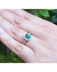 Women's 14K white gold ring with a cushion-cut emerald and diamond halo, worn on a hand.