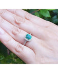 Women's 14K white gold ring with a cushion-cut emerald and diamond halo, worn on a hand.