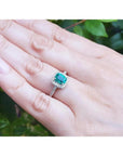 Women's 14K white gold ring with a cushion-cut emerald and diamond halo, worn on a hand.