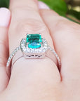 Natural emerald rings for women with diamond accents on a finger against a blurred green background.