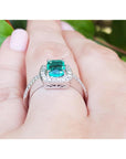 Natural emerald rings for women with diamond accents on a finger against a blurred green background.