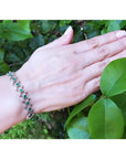 14K white gold bracelet with round Colombian emeralds bezel-set in diamond-shaped links on a woman's wrist.