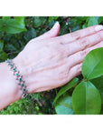 14K white gold bracelet with round Colombian emeralds bezel-set in diamond-shaped links on a woman's wrist.