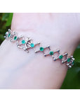 14K white gold bracelet with round Colombian emeralds bezel-set in diamond-shaped links on a wrist.