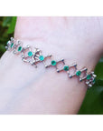 14K white gold bracelet with round Colombian emeralds bezel-set in diamond-shaped links on a wrist.