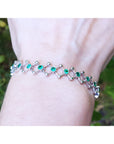 Emerald bracelet for women round cut natural Colombian emeralds 14k white gold on a wrist against a natural background.