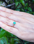 Hand wearing a natural emerald and baguette diamond ring against a natural background.
