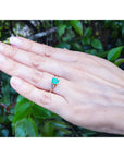 Hand wearing a natural emerald and baguette diamond ring against a natural background.
