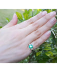 1.56 ct. emerald ring with princess-cut side diamonds in 14K white gold on a hand.