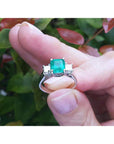 Natural Colombian emerald rings held between fingers against a blurred natural background.