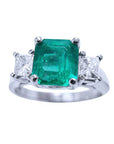 A top side view of an emerald and princess cut side diamonds ring in white gold.