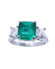 A top side view of an emerald and princess cut side diamonds ring in white gold.