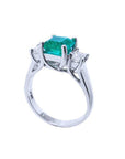 An emerald engagement ring with princess cut side diamonds on its half side profile, displaying the top and gallery.