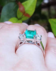 Natural emerald rings on a hand with a blurred green leafy background.