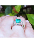 Natural emerald rings on a hand with a blurred green leafy background.