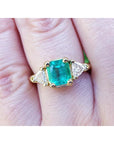 A 18k yellow gold colombian emerald ring with side trillion cut natural diamonds on a finger.