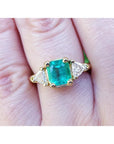 A 18k yellow gold colombian emerald ring with side trillion cut natural diamonds on a finger.