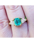 A 18k yellow gold colombian emerald ring with side trillion cut natural diamonds on a finger.