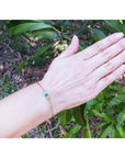 Woman's hand wearing a delicate 14K yellow gold solitaire bracelet with a deep green emerald.