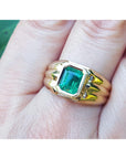 A yellow gold men's emerald solitaire ring on a finger.