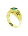 A yellow gold men's emerald ring showing the top bezel setting and partial lateral side band design.