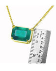 Emerald-cut Colombian emerald solitaire necklace in 18K yellow gold, shown with a ruler for scale.