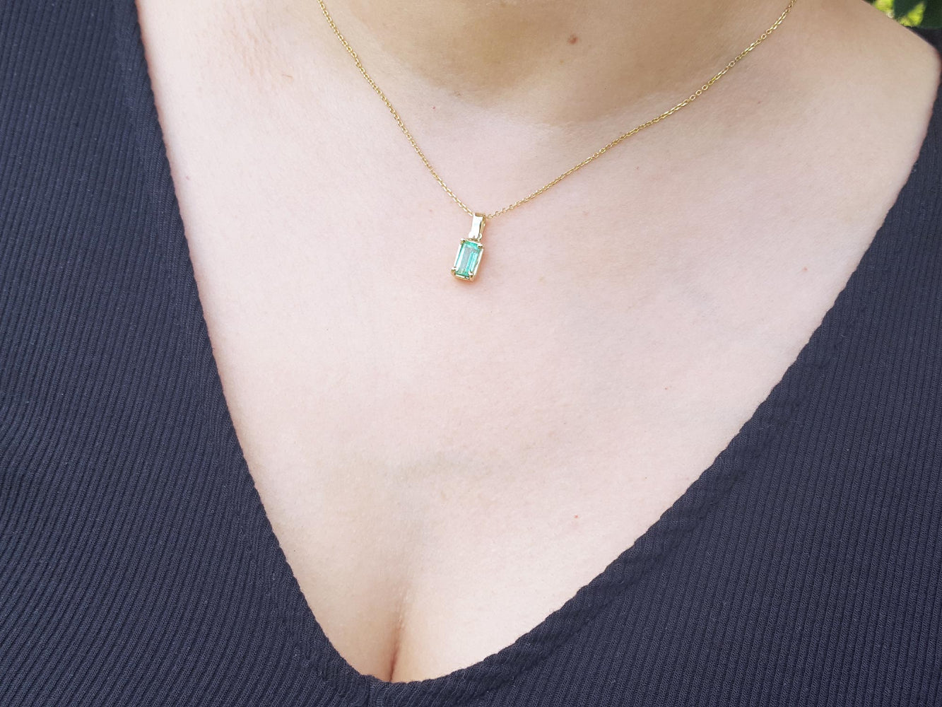 Necklace with a solitaire emerald pendant on a person wearing a dark blue top.